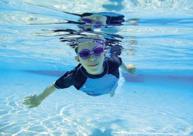 A child smiling underwater in a swimming pool, on holiday.
